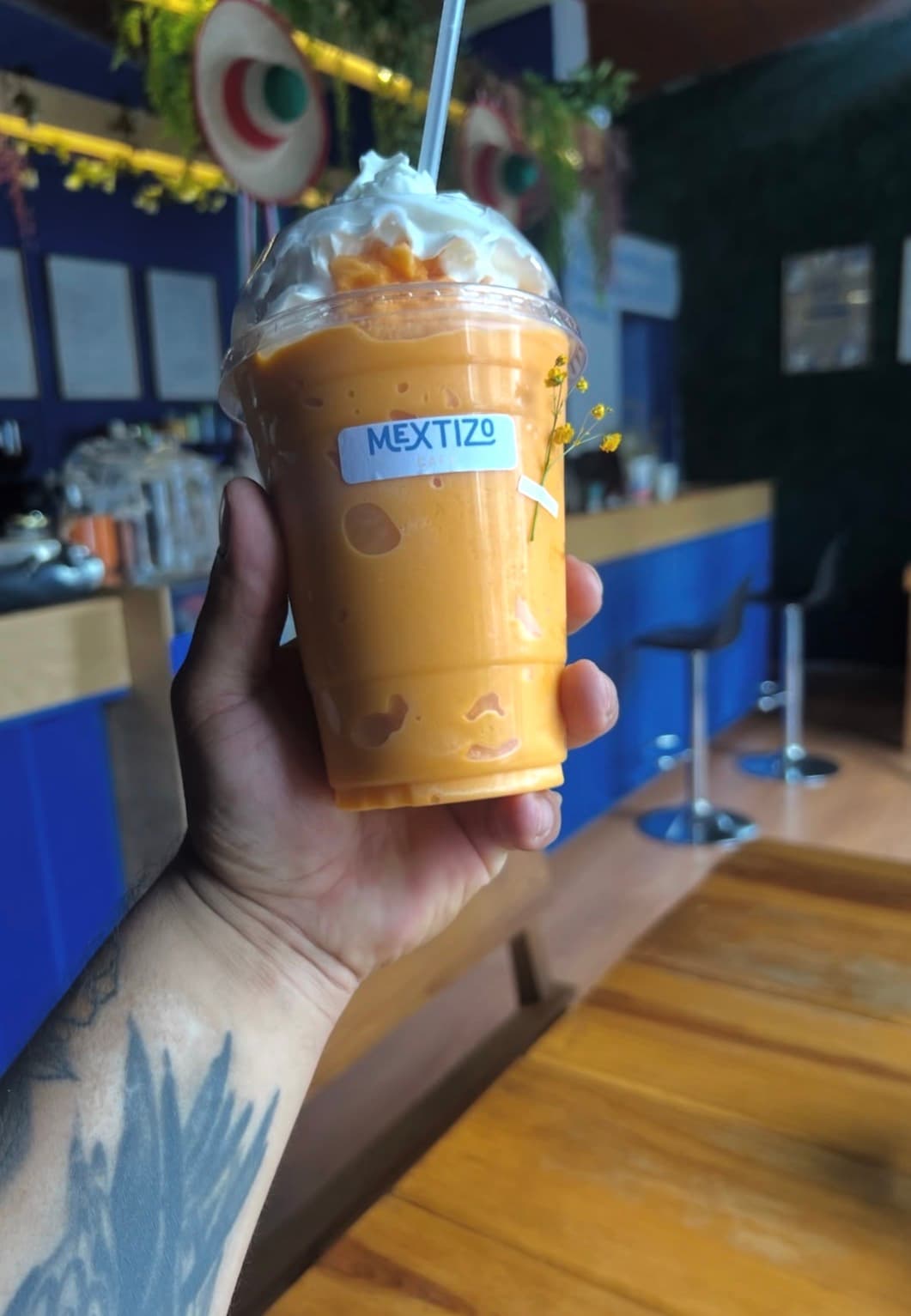 Bebida frappé con crema batida en vaso con tapa, sostenida frente a la barra