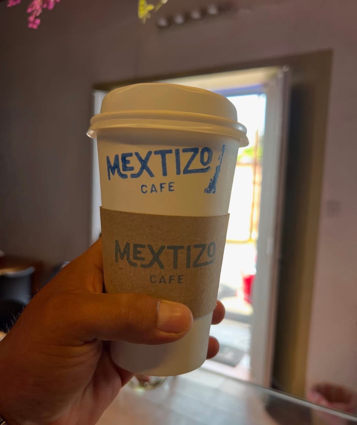 Vaso para llevar de Mextizo Café sostenido junto a la entrada del local