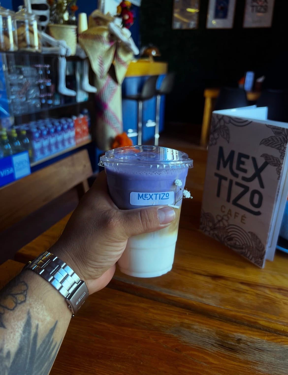 Taro Frappé de color morado en vaso con tapa, con el menú de Mextizo Café al fondo